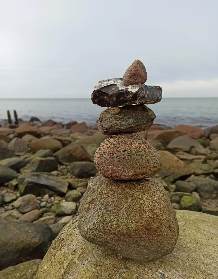 Aufeinandergeschichtete Steine an der Küste, Sinnbild für Balance und das eigene Tempo